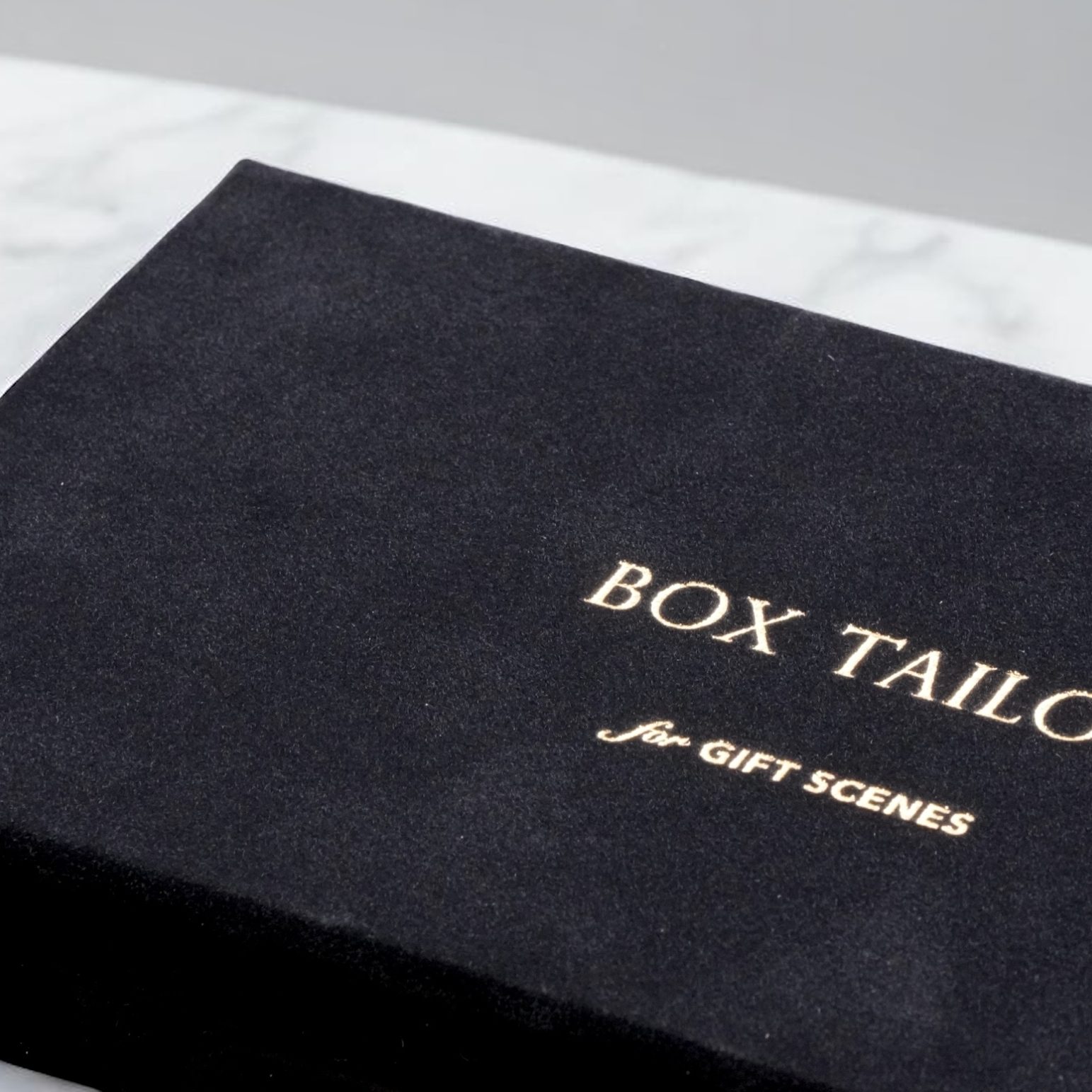 黒スエード紙を使用した高級ギフト向け貼り箱。BOX TAILORの金箔押しロゴが入ったヒンジ型パッケージの外観。